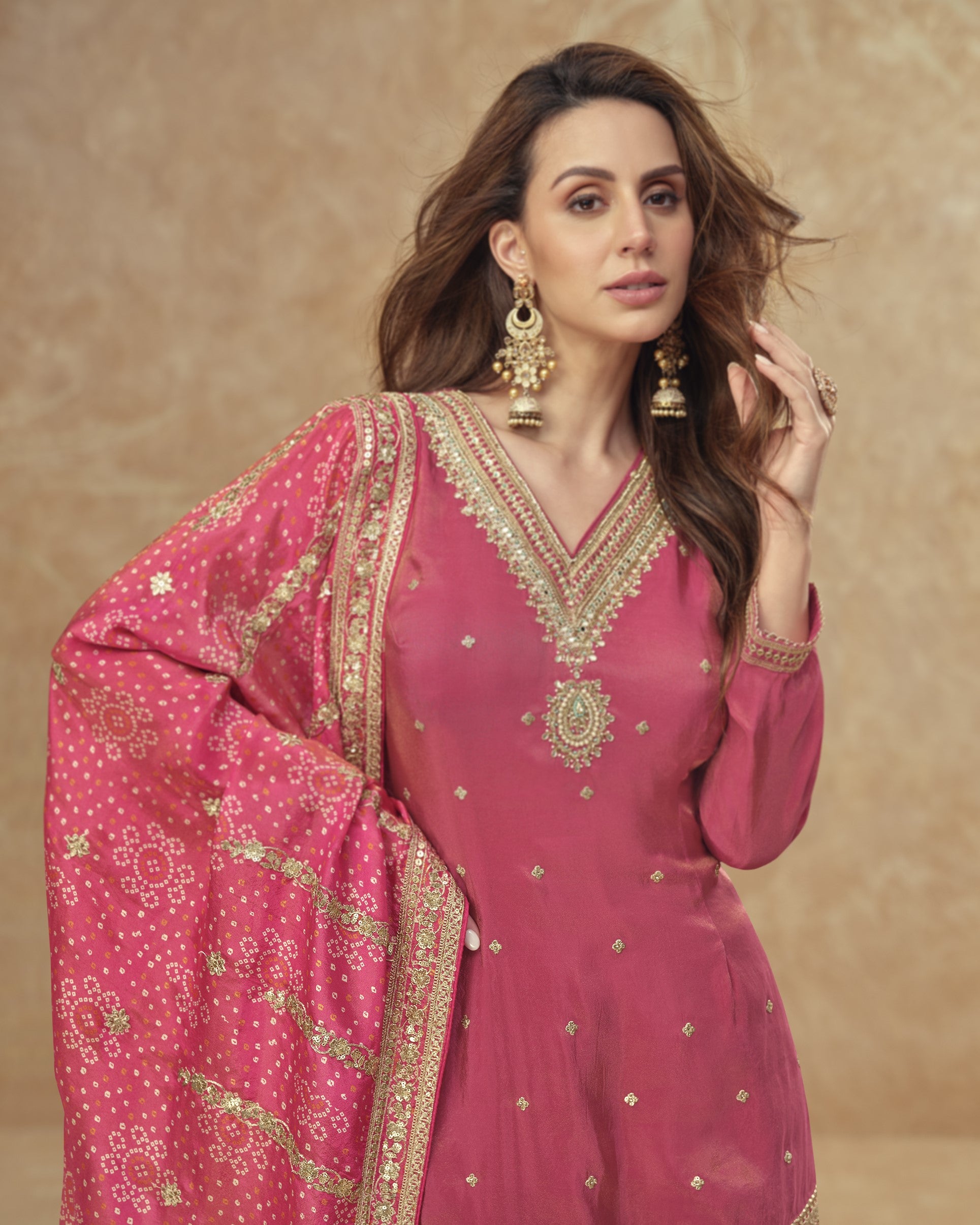 Woman wearing a pink traditional outfit with gold embroidery on a beige background