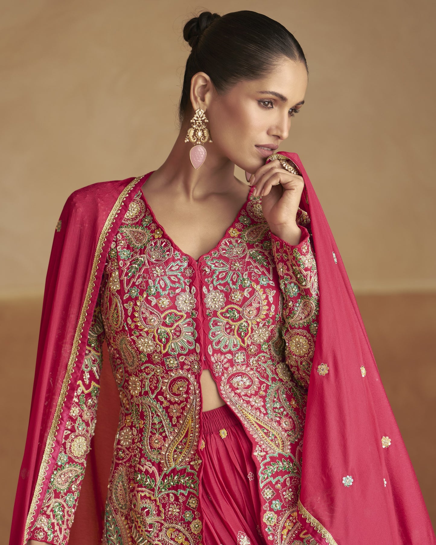 Woman wearing a traditional pink and gold embroidered outfit with a beige background