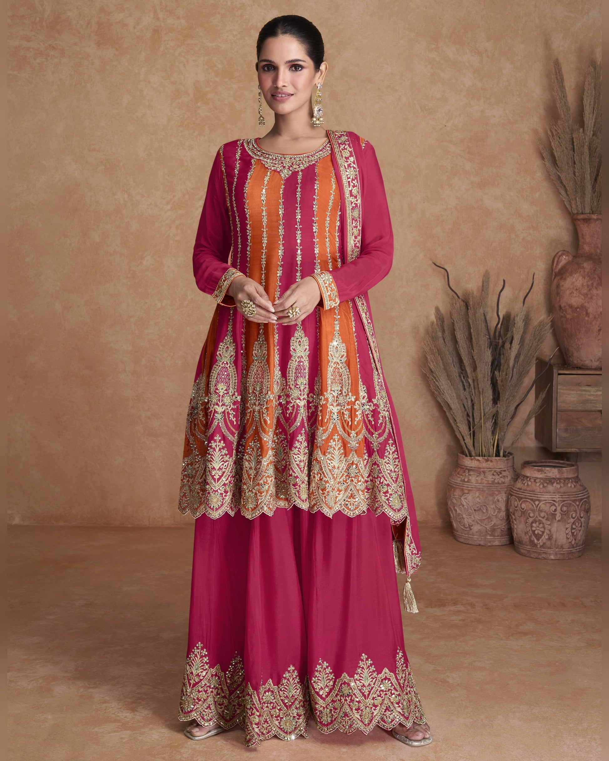 Woman wearing a pink traditional outfit with intricate patterns in a warm-toned room.