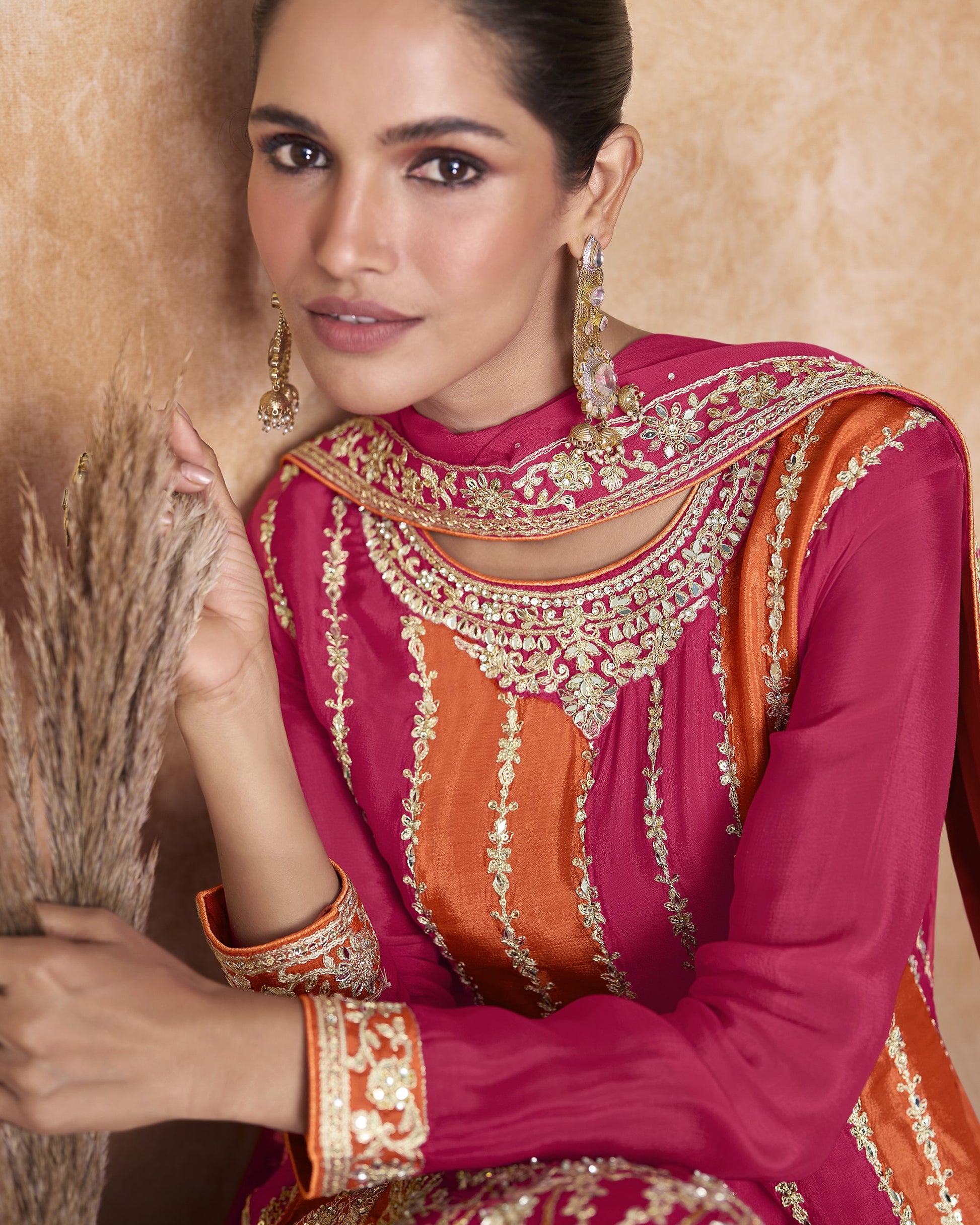 Woman wearing a pink and orange embroidered traditional outfit with a beige background