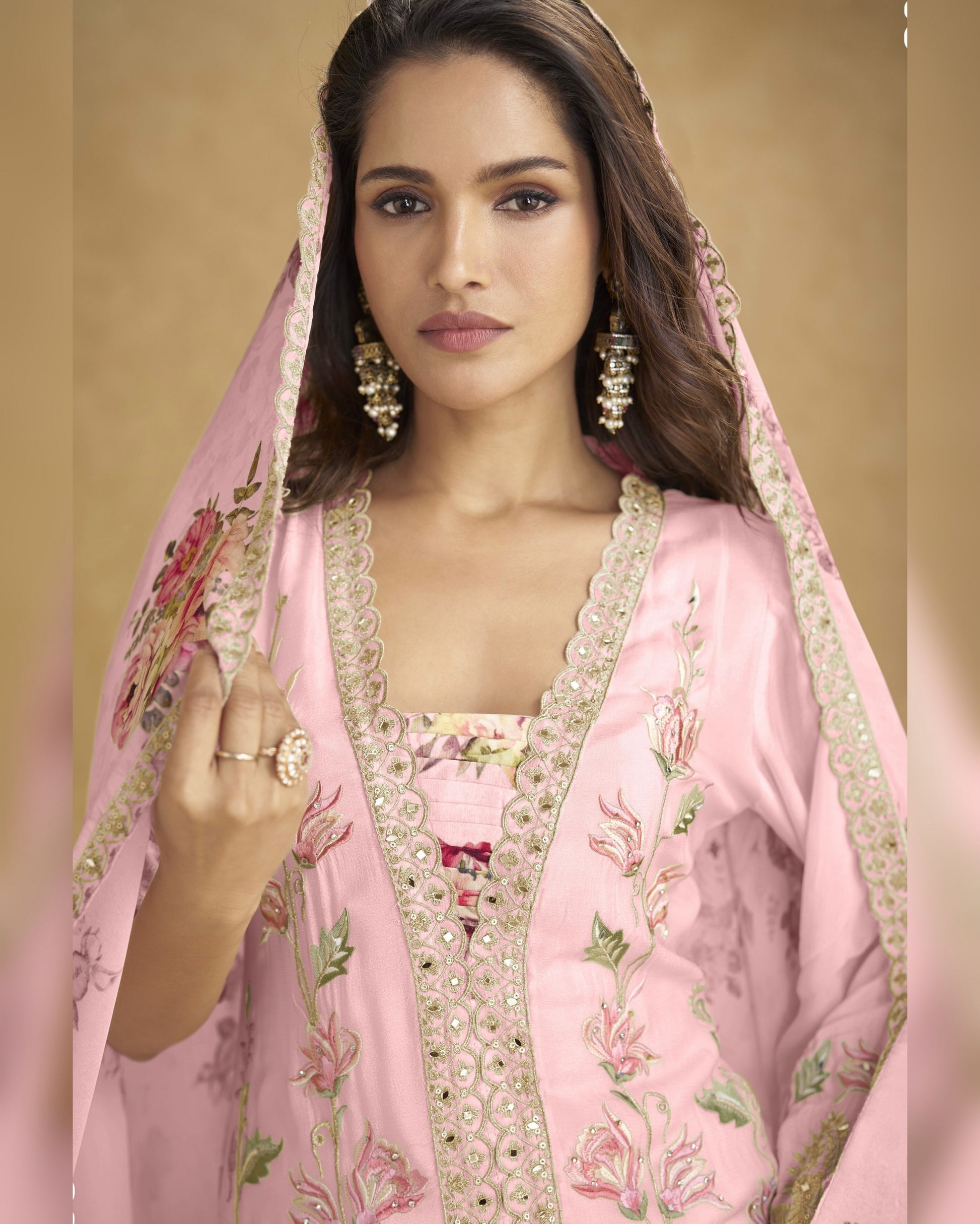Woman wearing a pink embroidered traditional outfit with a matching dupatta.