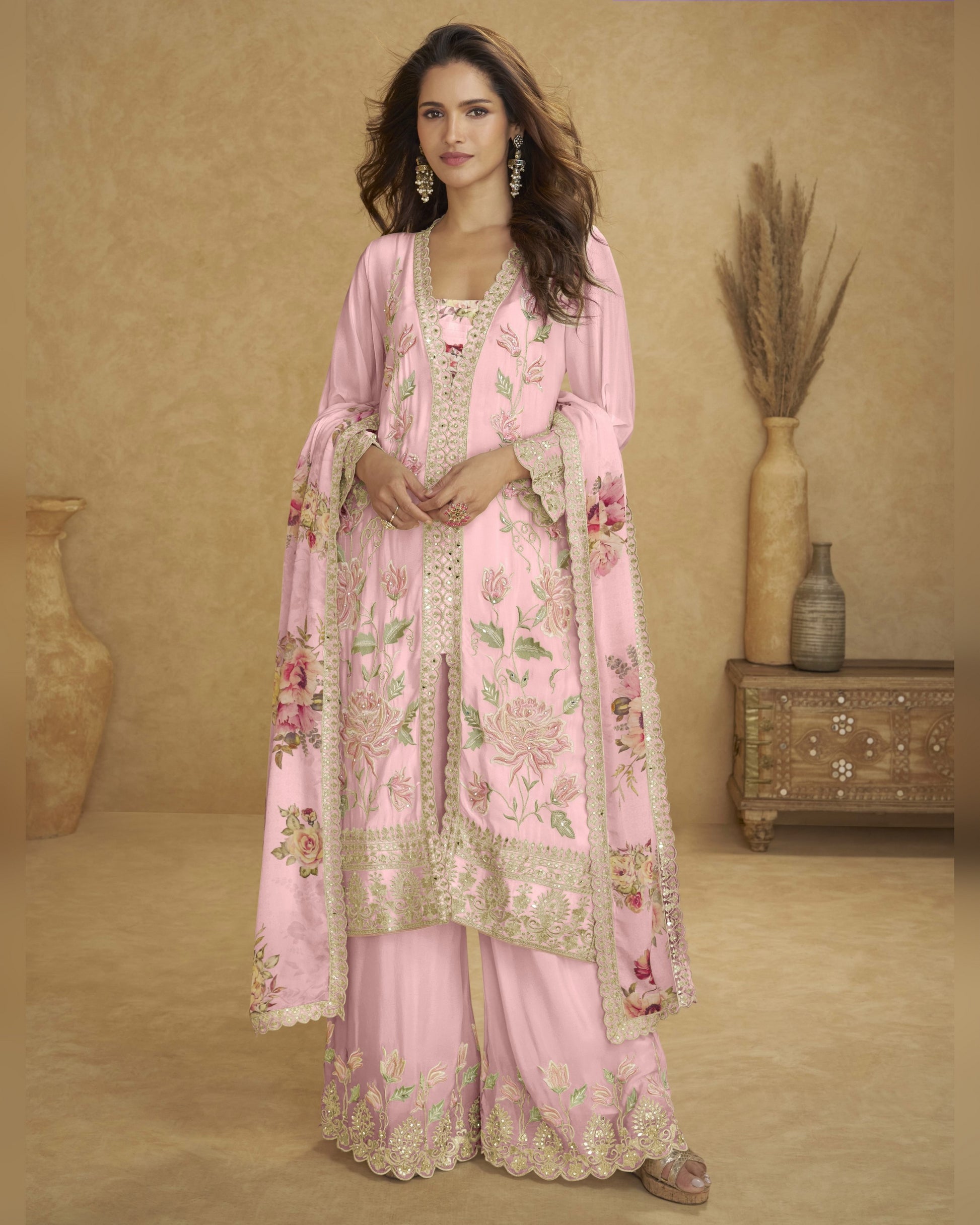 Woman wearing a pink embroidered traditional outfit with a matching dupatta in a room setting.