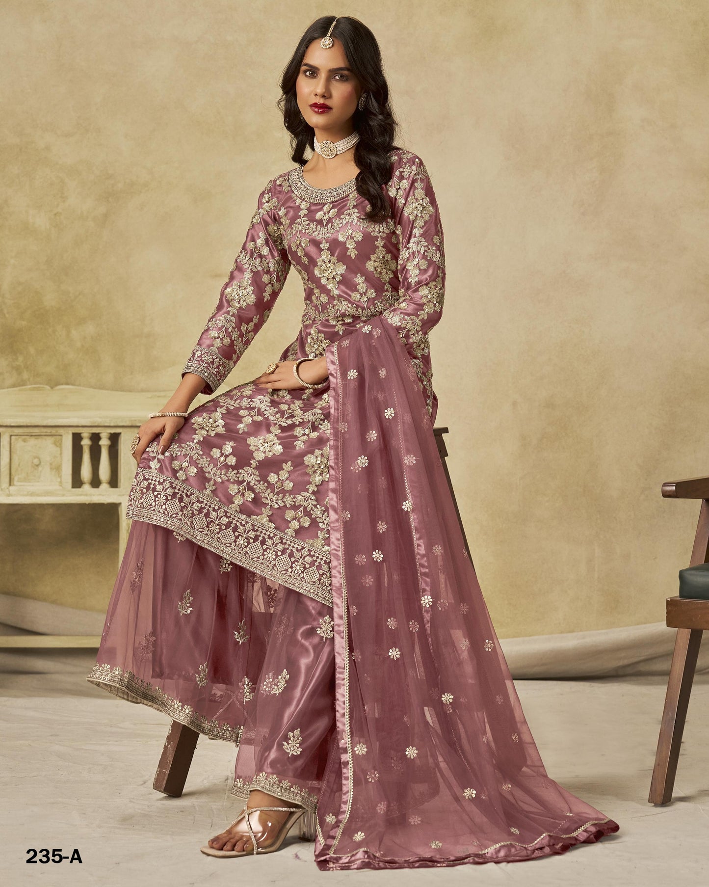 Woman wearing a mauve embroidered traditional outfit with a beige background