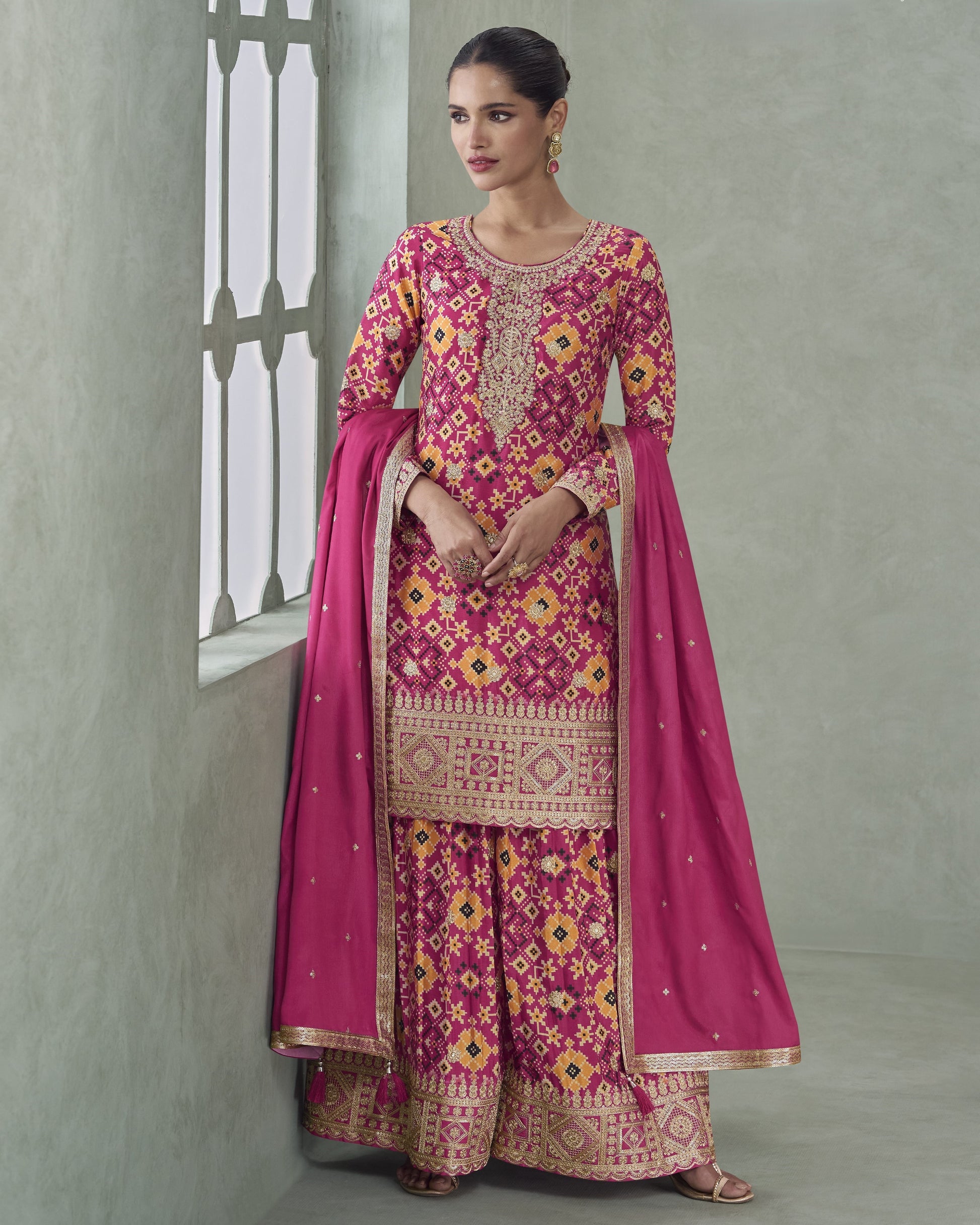 Woman wearing a traditional pink and gold embroidered outfit with a matching dupatta against a neutral background.