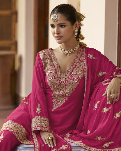 Woman in a pink embroidered traditional outfit with gold jewelry indoors.