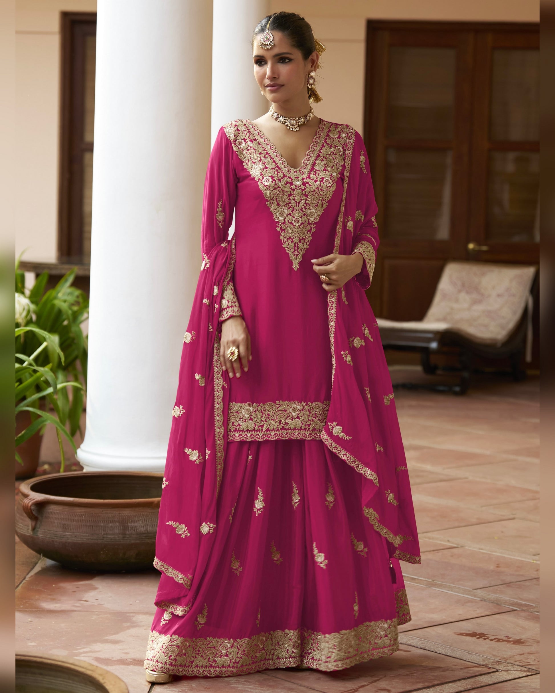 Woman wearing a pink traditional outfit with gold embroidery in an indoor setting.