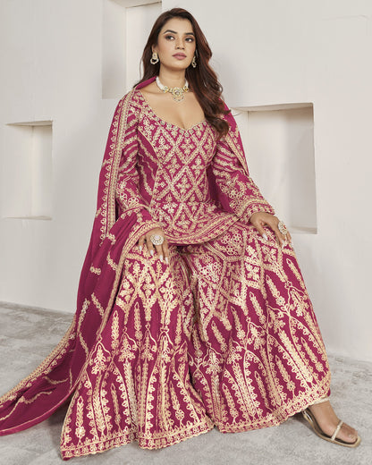 Woman wearing a traditional maroon and gold embroidered outfit in a minimalistic setting