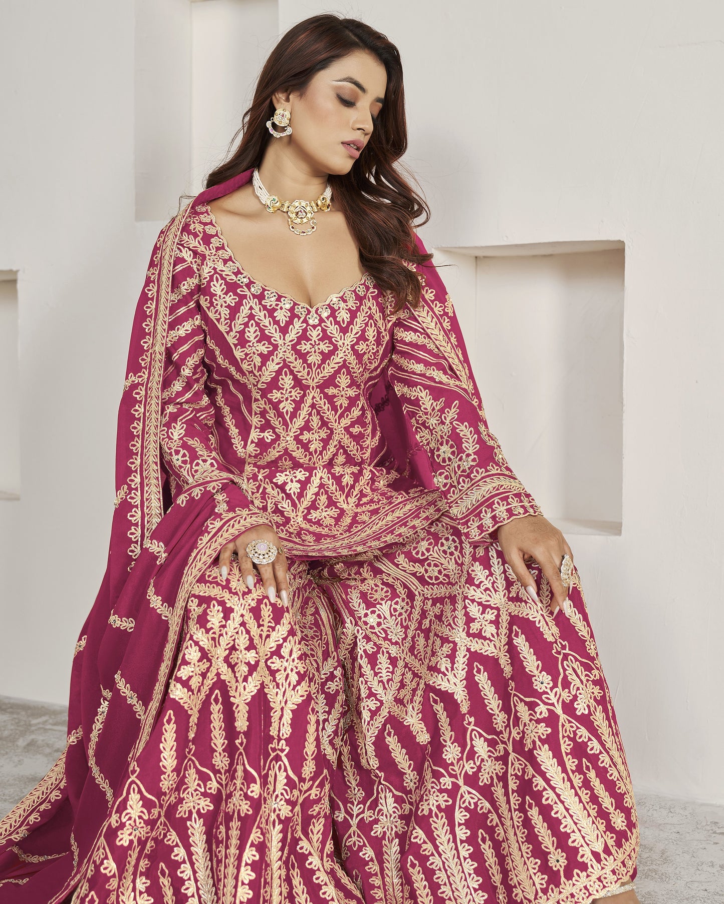 Woman in a traditional embroidered pink and gold outfit against a white background