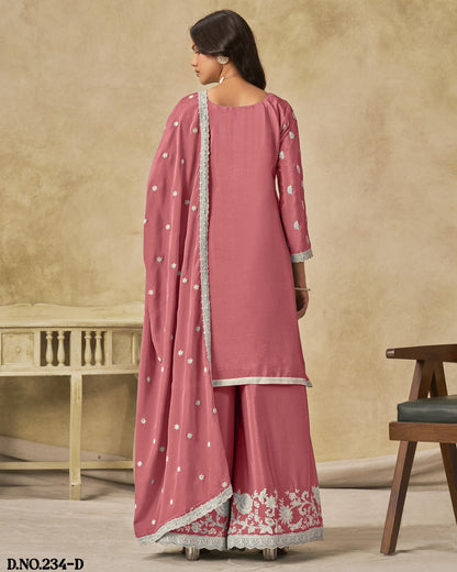 Woman wearing a pink traditional outfit with white patterns in a room setting.