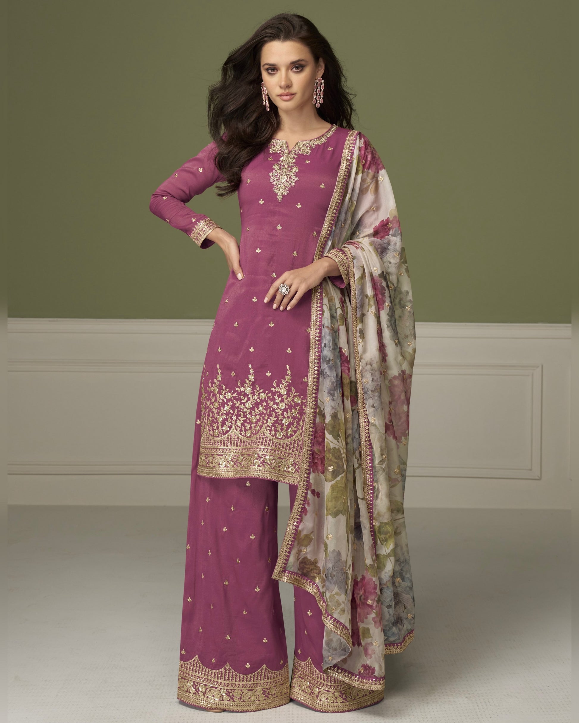 Woman wearing a traditional outfit with a purple dress and floral dupatta on a plain background