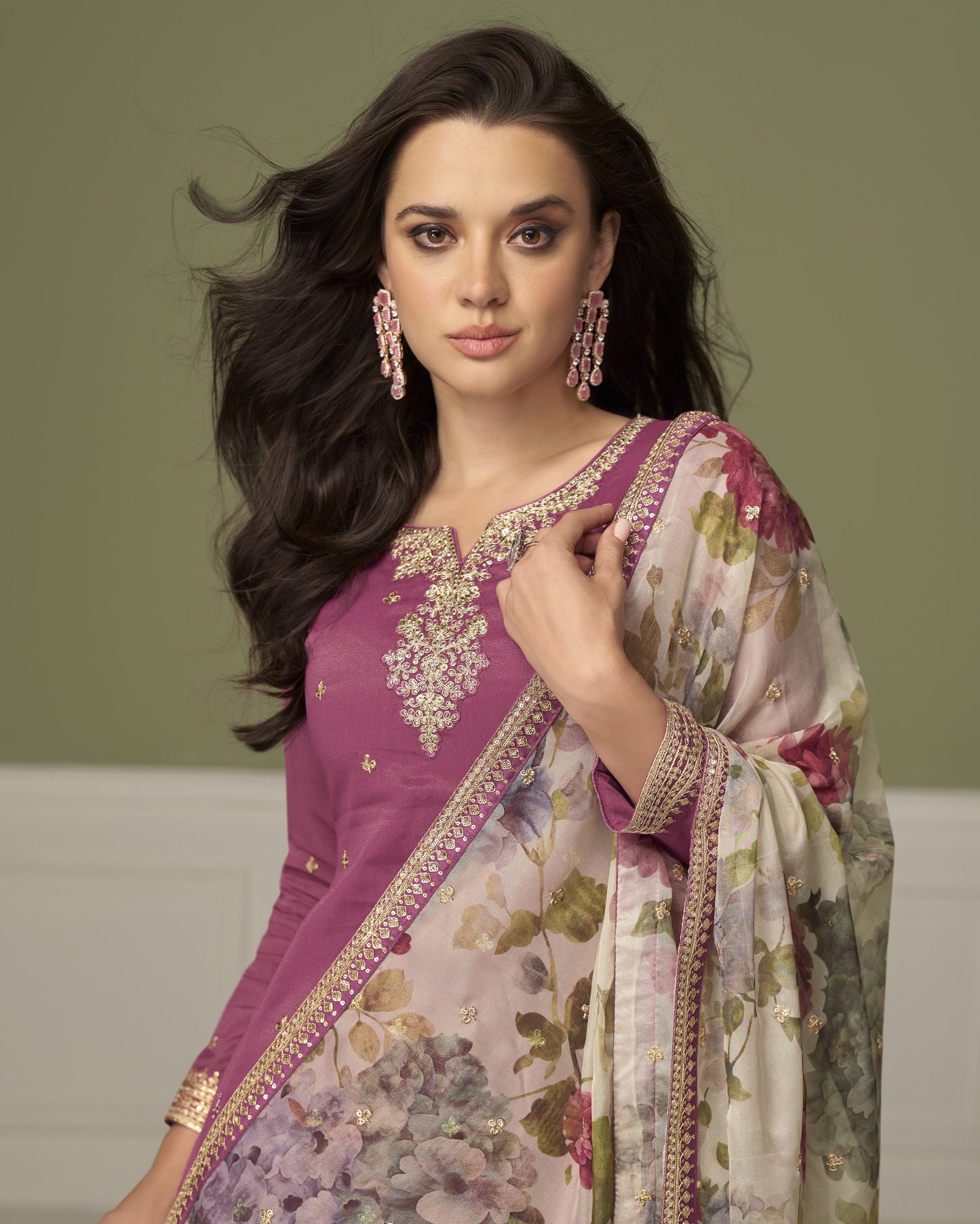 Woman wearing a traditional outfit with a floral pattern against a plain background