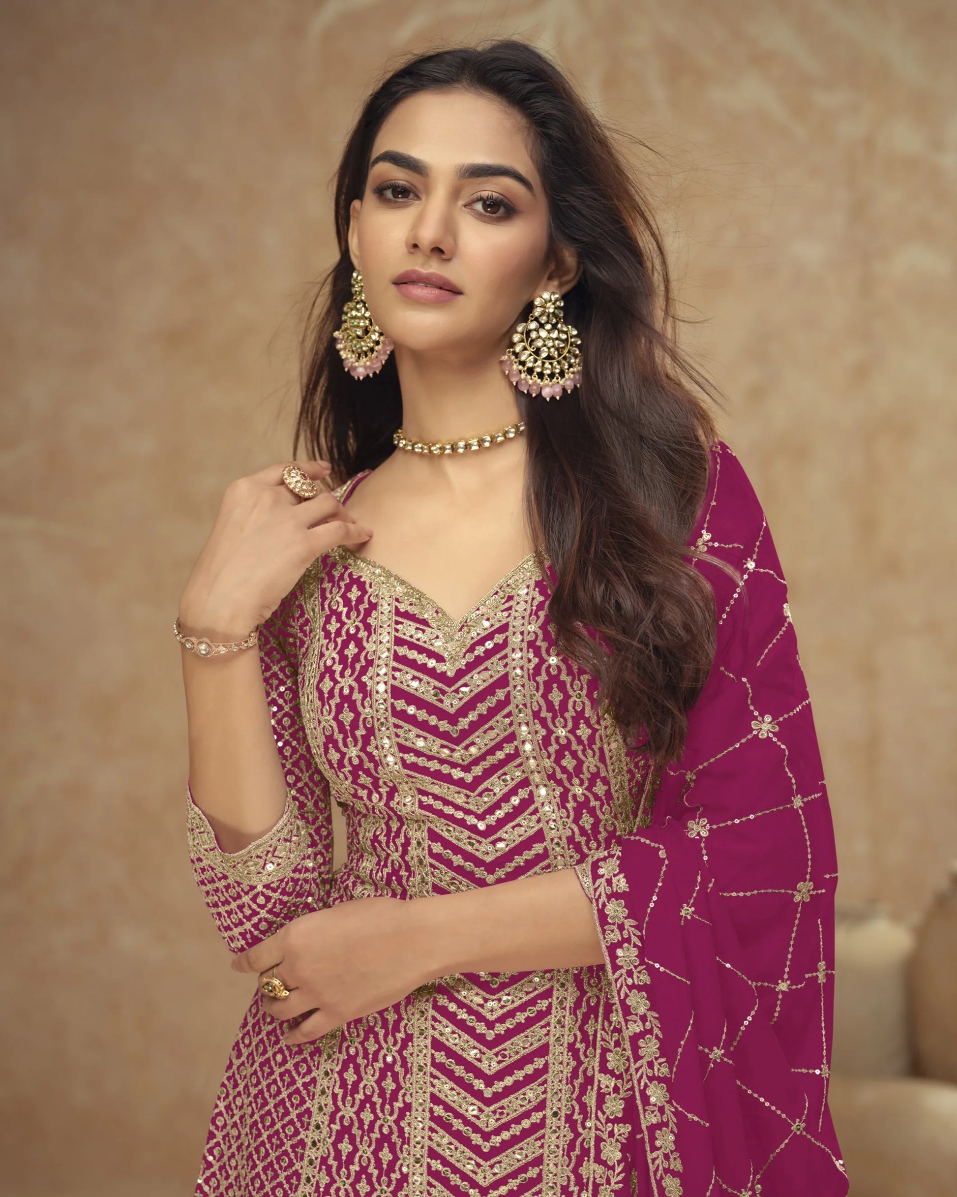 Woman in a traditional outfit with intricate patterns and jewelry against a beige background
