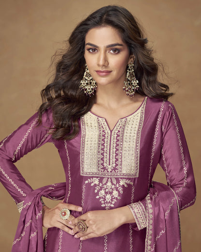 Woman wearing a purple embroidered traditional outfit with gold jewelry on a brown background