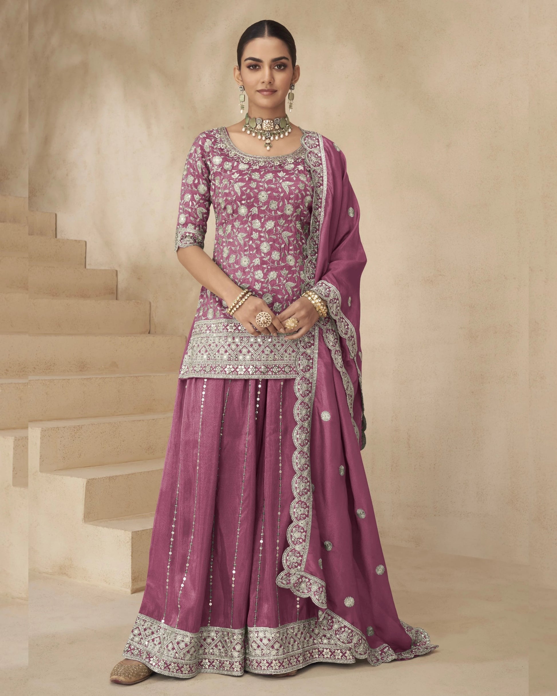 Woman in a traditional pink and silver embroidered outfit standing on a staircase.