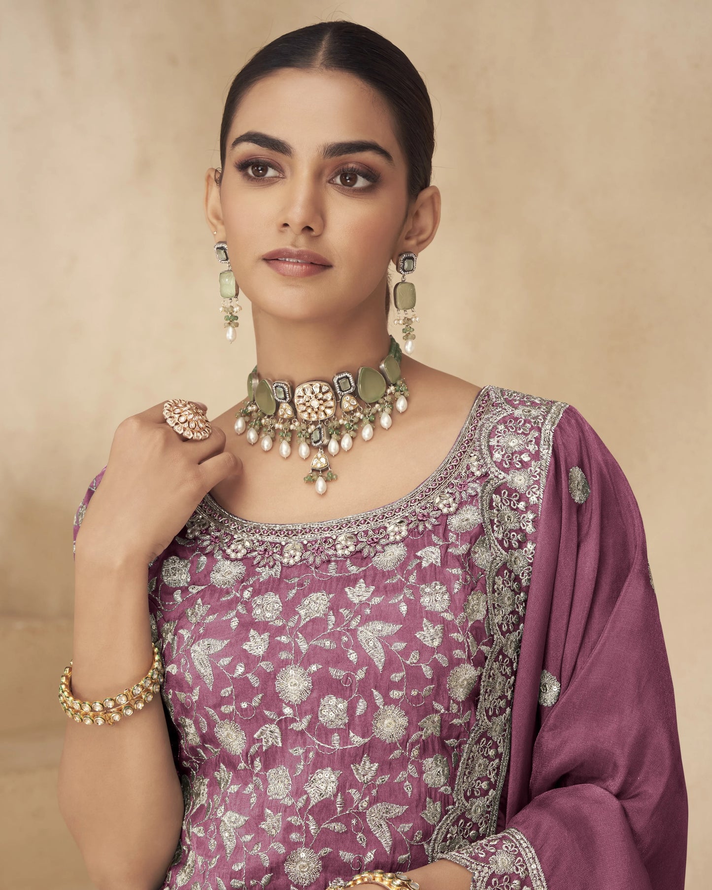 Woman wearing a purple saree with floral patterns and gold jewelry against a beige background