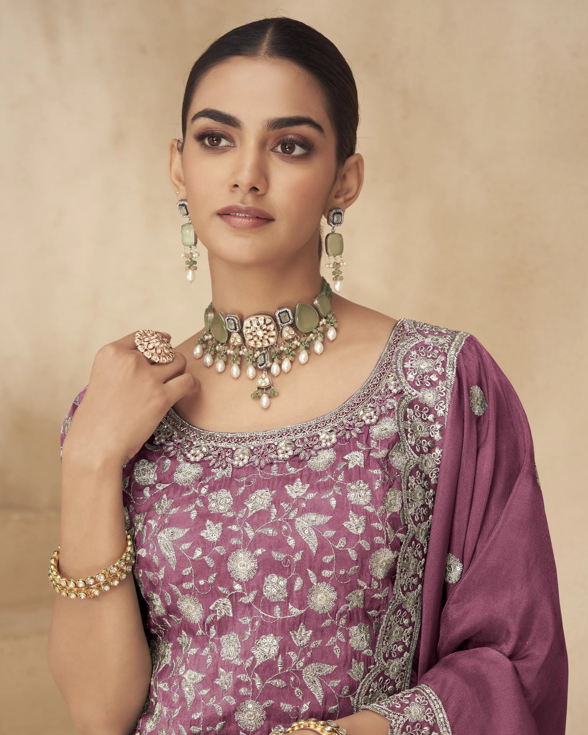 Woman wearing a purple saree with floral patterns and gold jewelry against a beige background