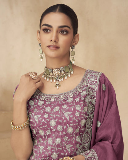 Woman wearing a purple saree with floral patterns and gold jewelry against a beige background
