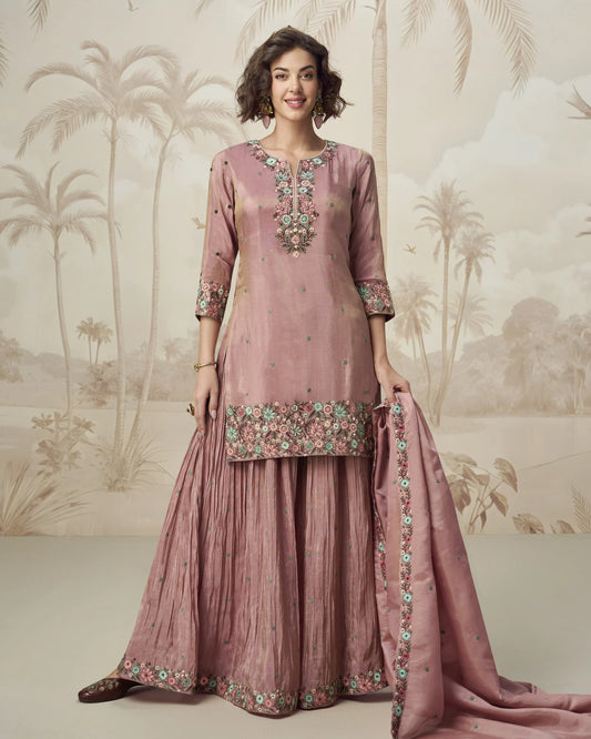 Woman wearing a pink traditional outfit with floral embroidery against a decorative background