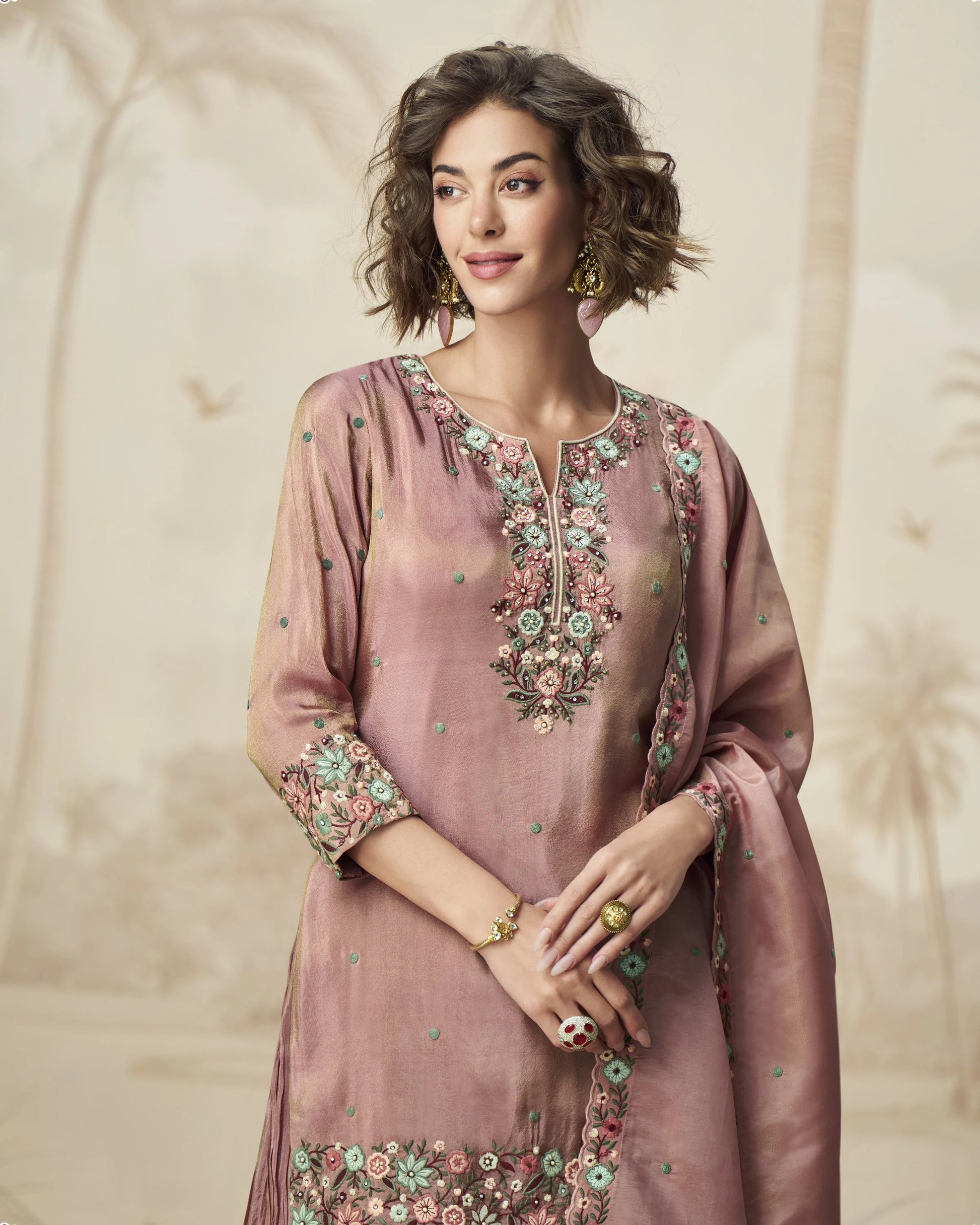 Woman wearing a pink embroidered traditional outfit against a beige background
