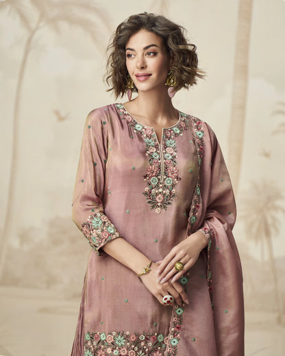 Woman wearing a pink embroidered traditional outfit against a beige background