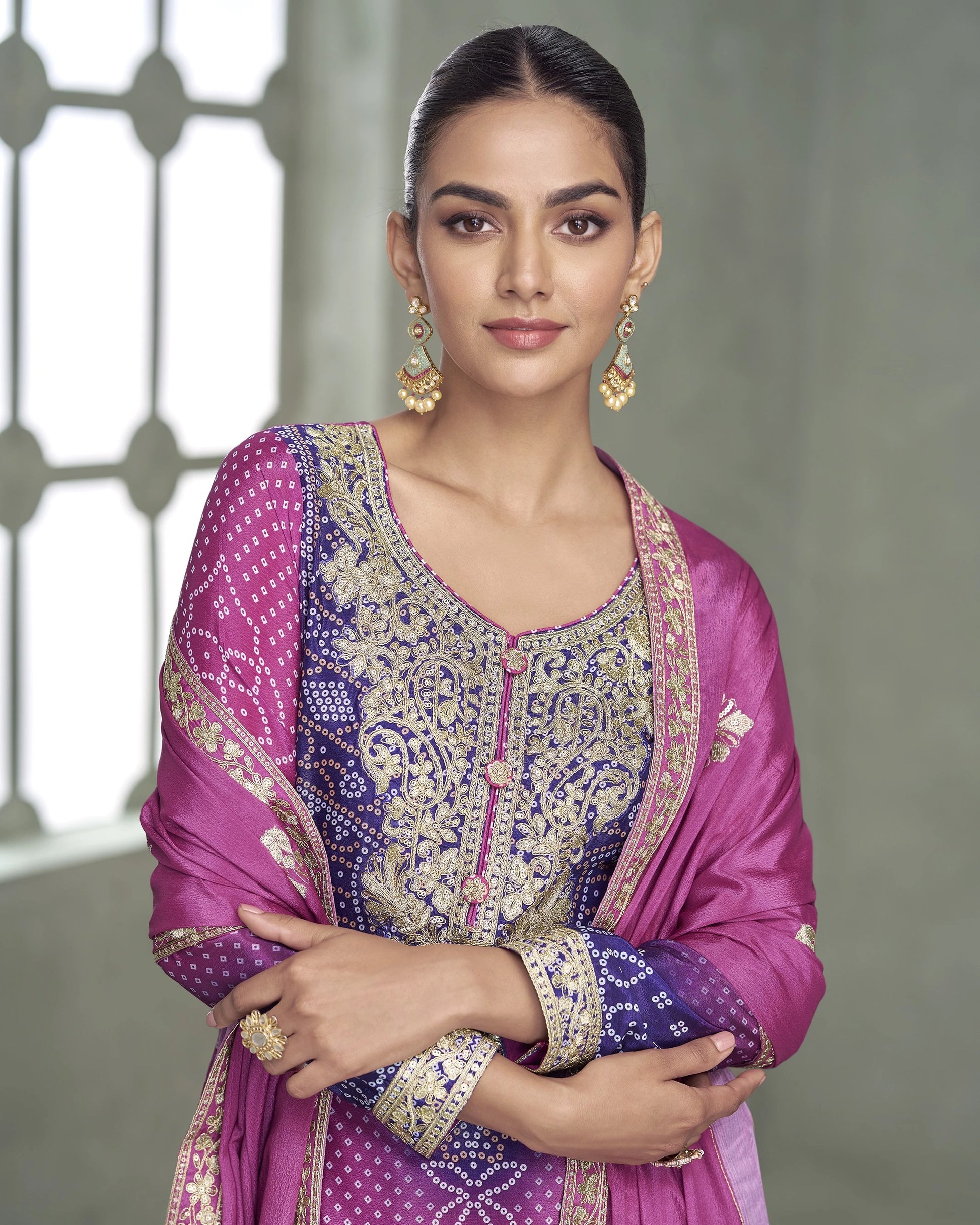 Woman wearing a traditional pink and purple outfit with intricate patterns, standing against a neutral background.
