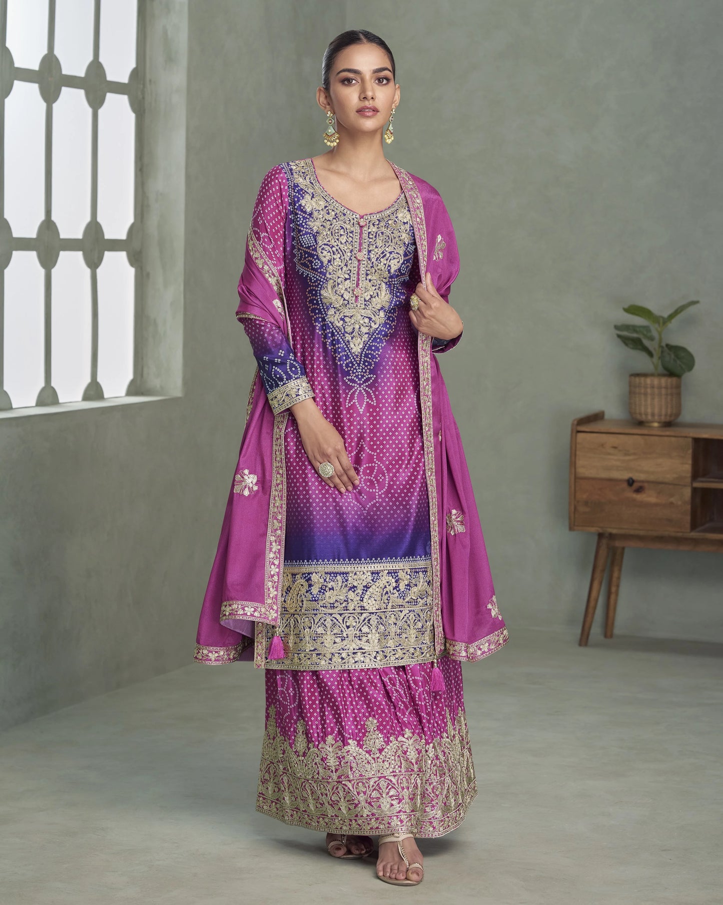 Woman wearing a traditional pink and purple embroidered outfit in a minimalistic room.