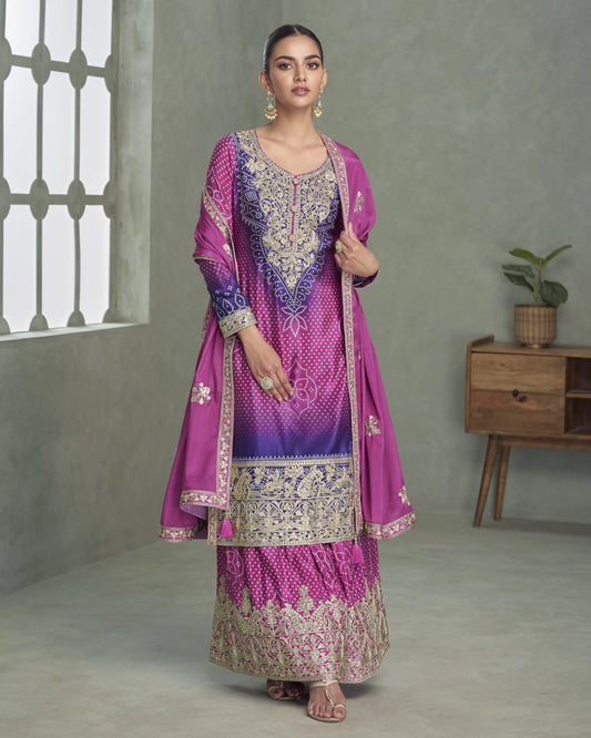 Woman wearing a traditional pink and purple embroidered outfit in a minimalistic room.