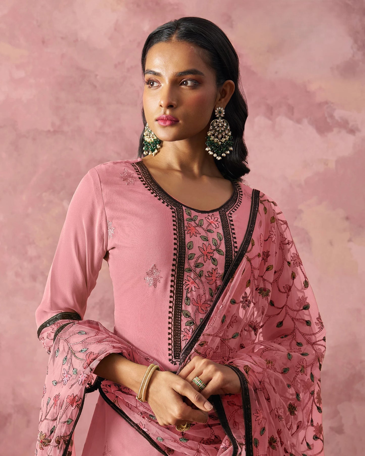 Woman wearing a pink traditional outfit with floral embroidery against a pink background