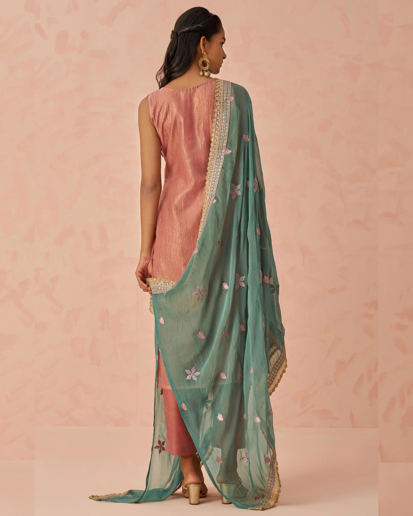 Woman wearing a pink saree with a green dupatta against a pink background