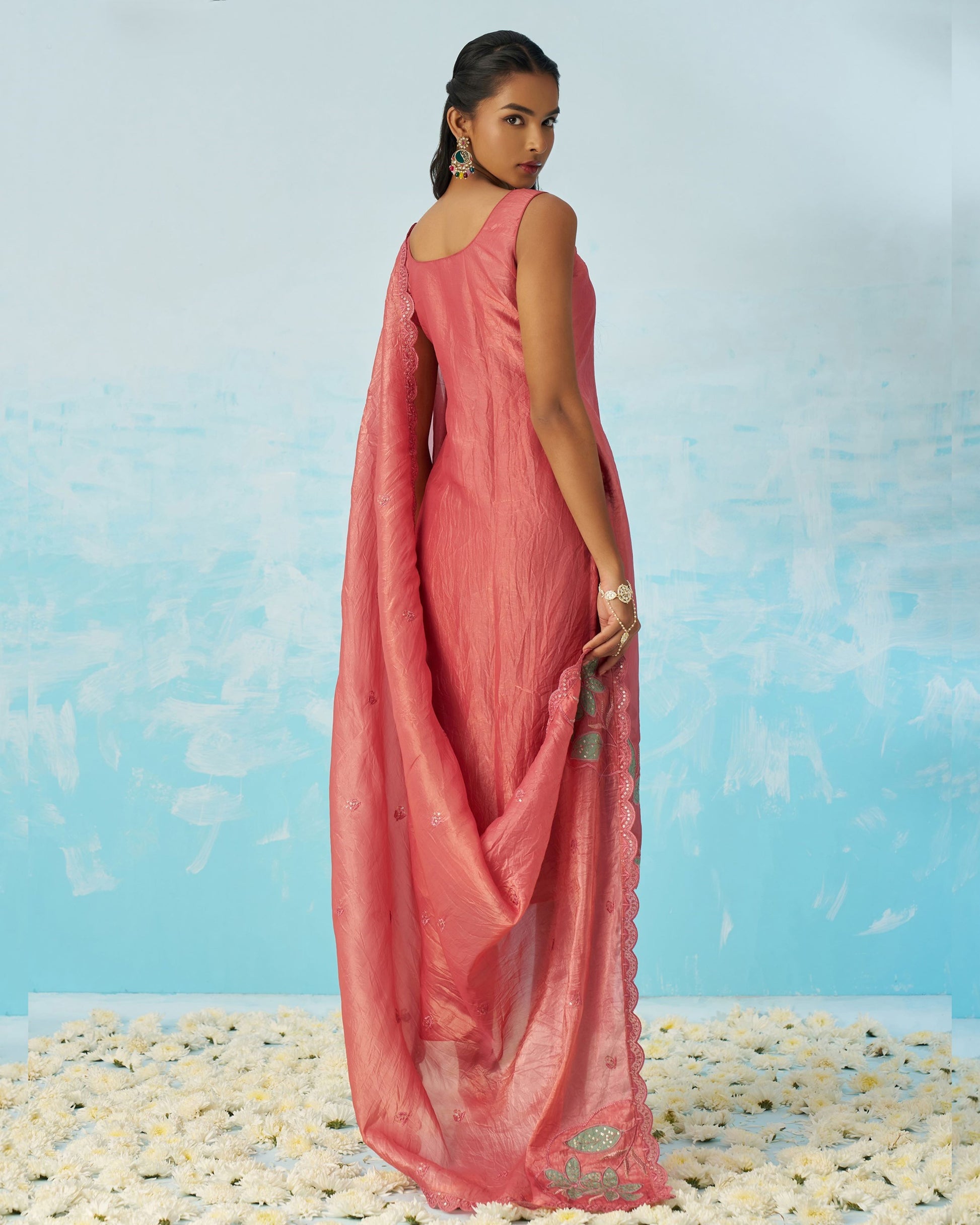 Woman in a pink saree standing on a pebbled surface with a blue background