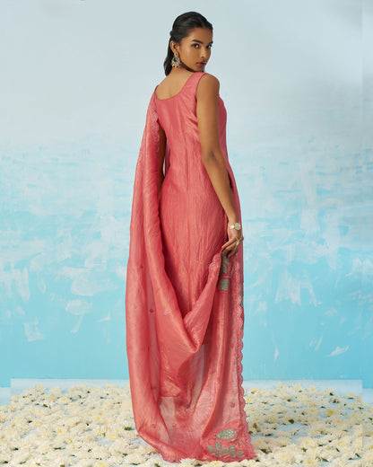 Woman in a pink saree standing on a pebbled surface with a blue background