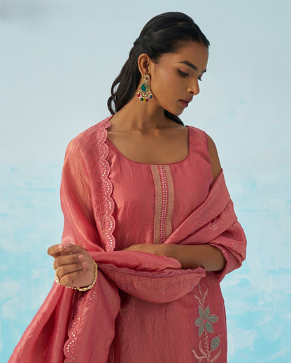 Woman wearing a pink traditional outfit with floral embroidery against a light blue background
