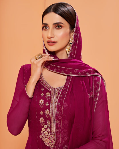 Woman wearing a magenta embroidered traditional outfit on a peach background