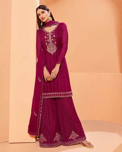 Woman wearing a magenta embroidered traditional outfit against a peach background
