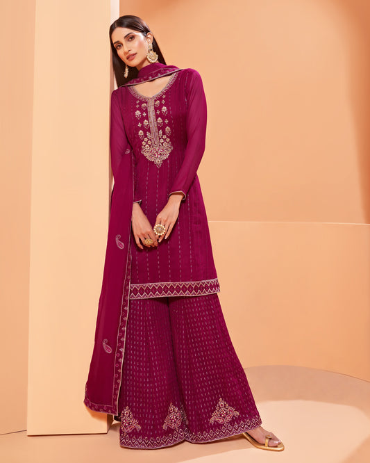 Woman wearing a magenta embroidered traditional outfit against a peach background
