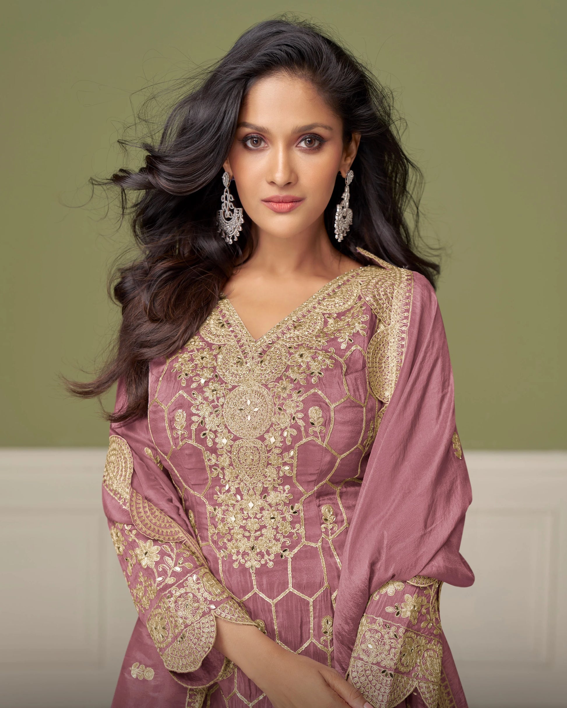 Woman wearing a traditional pink and gold embroidered outfit with a matching dupatta against a neutral background.
