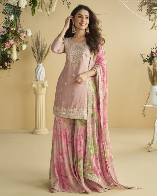 Woman in a traditional outfit with a pink and green dupatta in a decorated room.