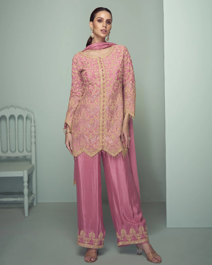 Woman wearing a pink embroidered traditional outfit with a matching dupatta against a gray background.