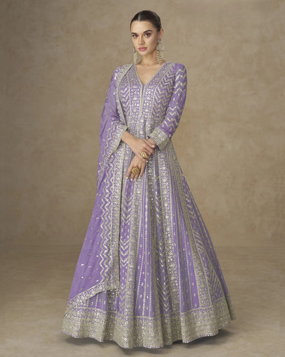 Woman wearing a purple and silver traditional outfit against a beige background