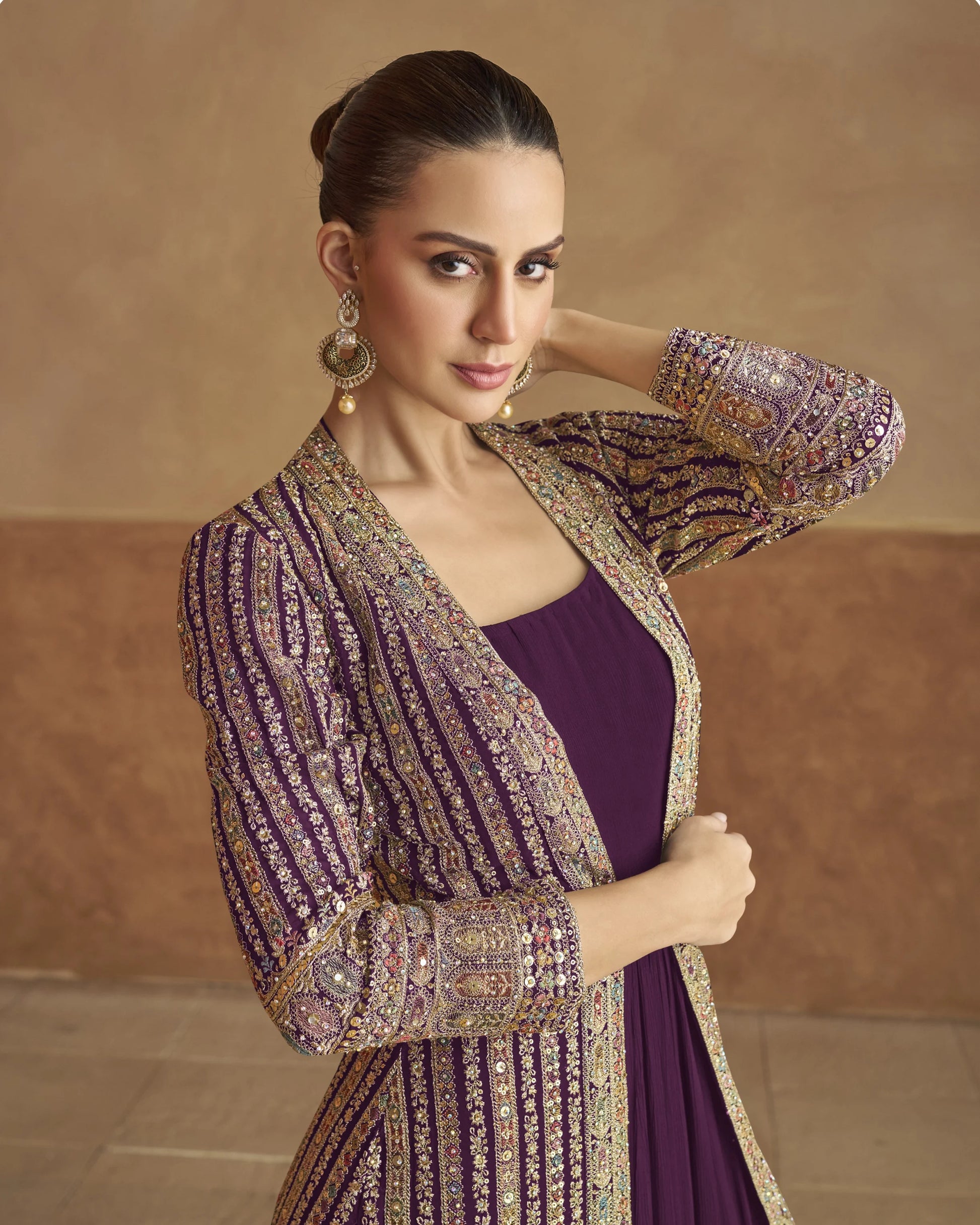 Woman wearing a traditional outfit with a purple dress and embroidered jacket against a beige background