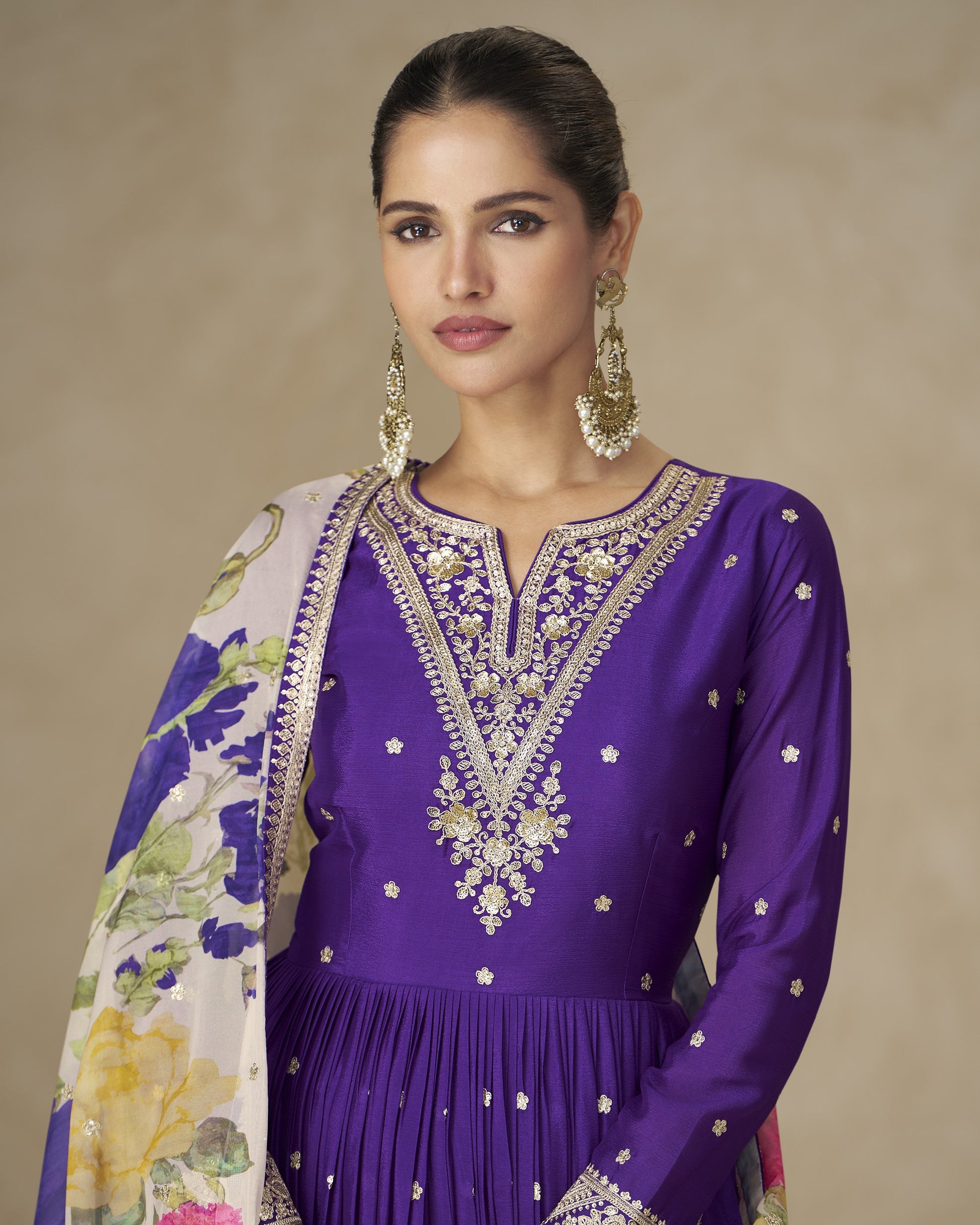 Woman wearing a purple embroidered outfit with a floral shawl against a beige background