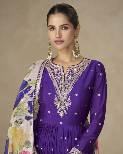 Woman wearing a purple embroidered outfit with a floral shawl against a beige background