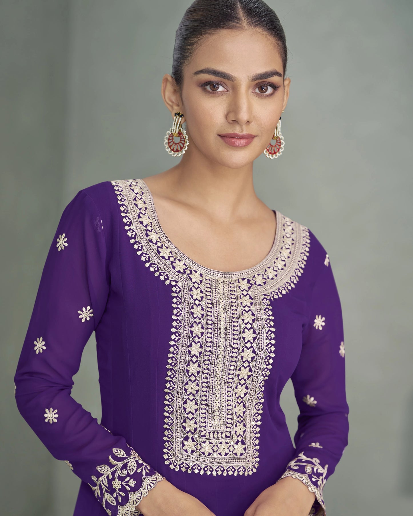 Woman wearing a purple traditional outfit with intricate white embroidery on a gray background