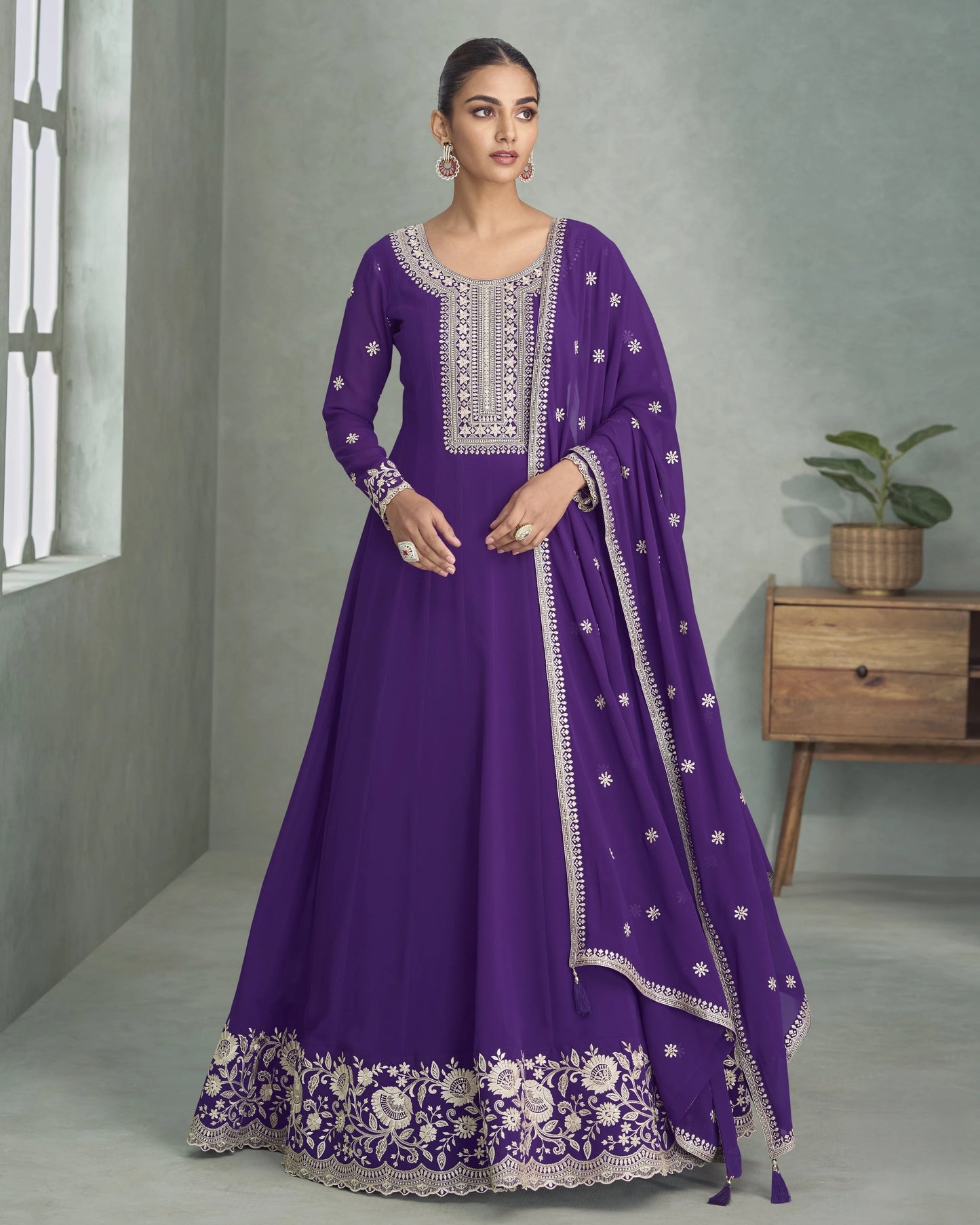 Woman wearing a purple traditional outfit with white embroidery in a room setting.