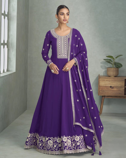 Woman wearing a purple traditional outfit with white embroidery in a room setting.