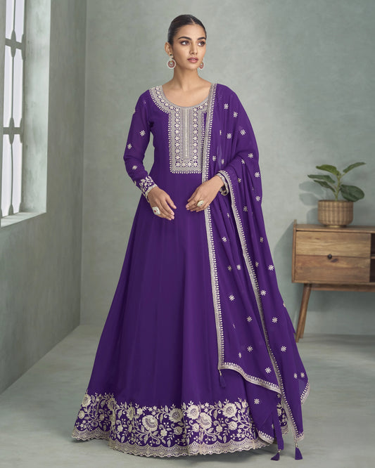 Woman wearing a purple traditional outfit with white embroidery in a room setting.