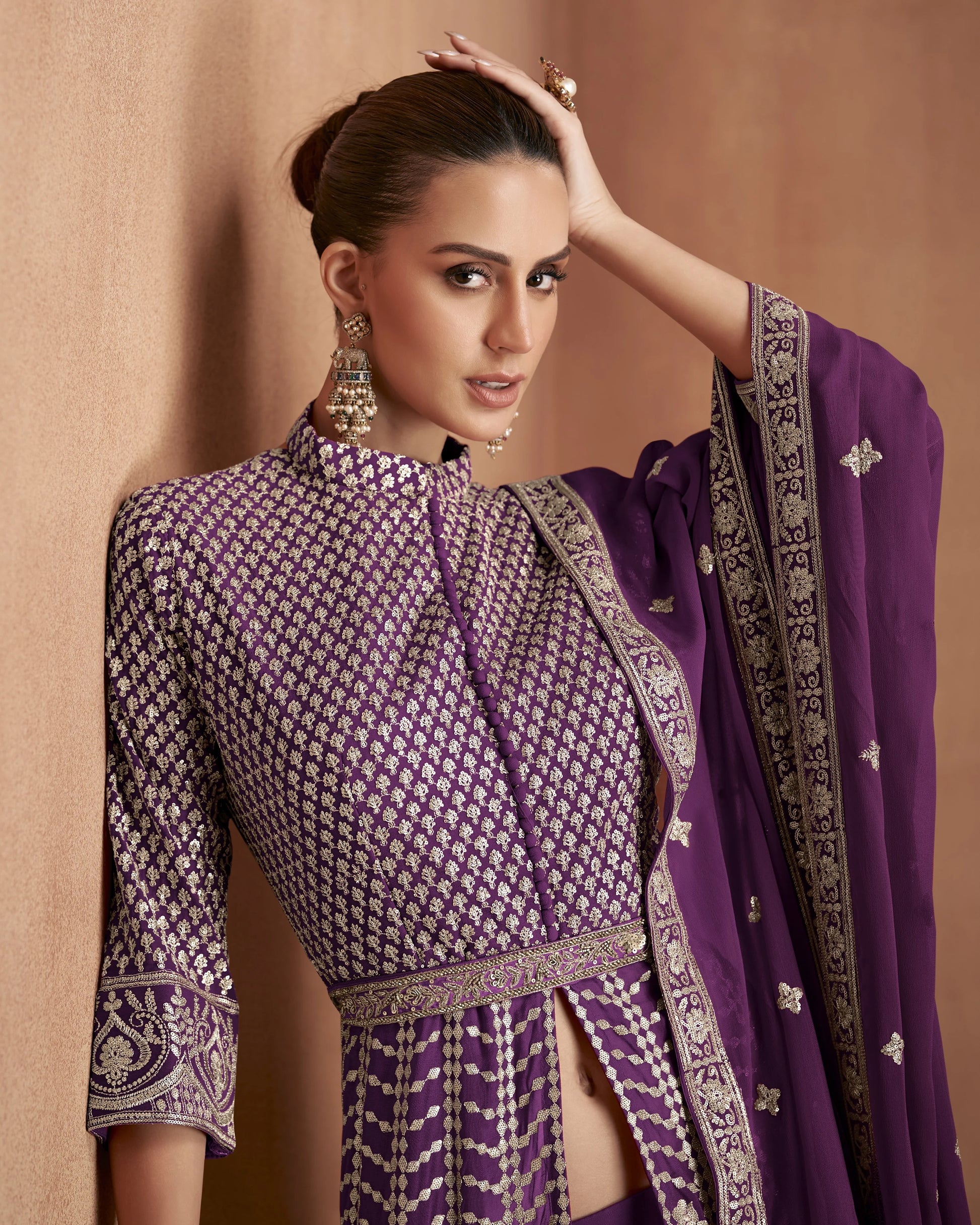 Woman in a traditional purple and black outfit with intricate patterns against a beige background