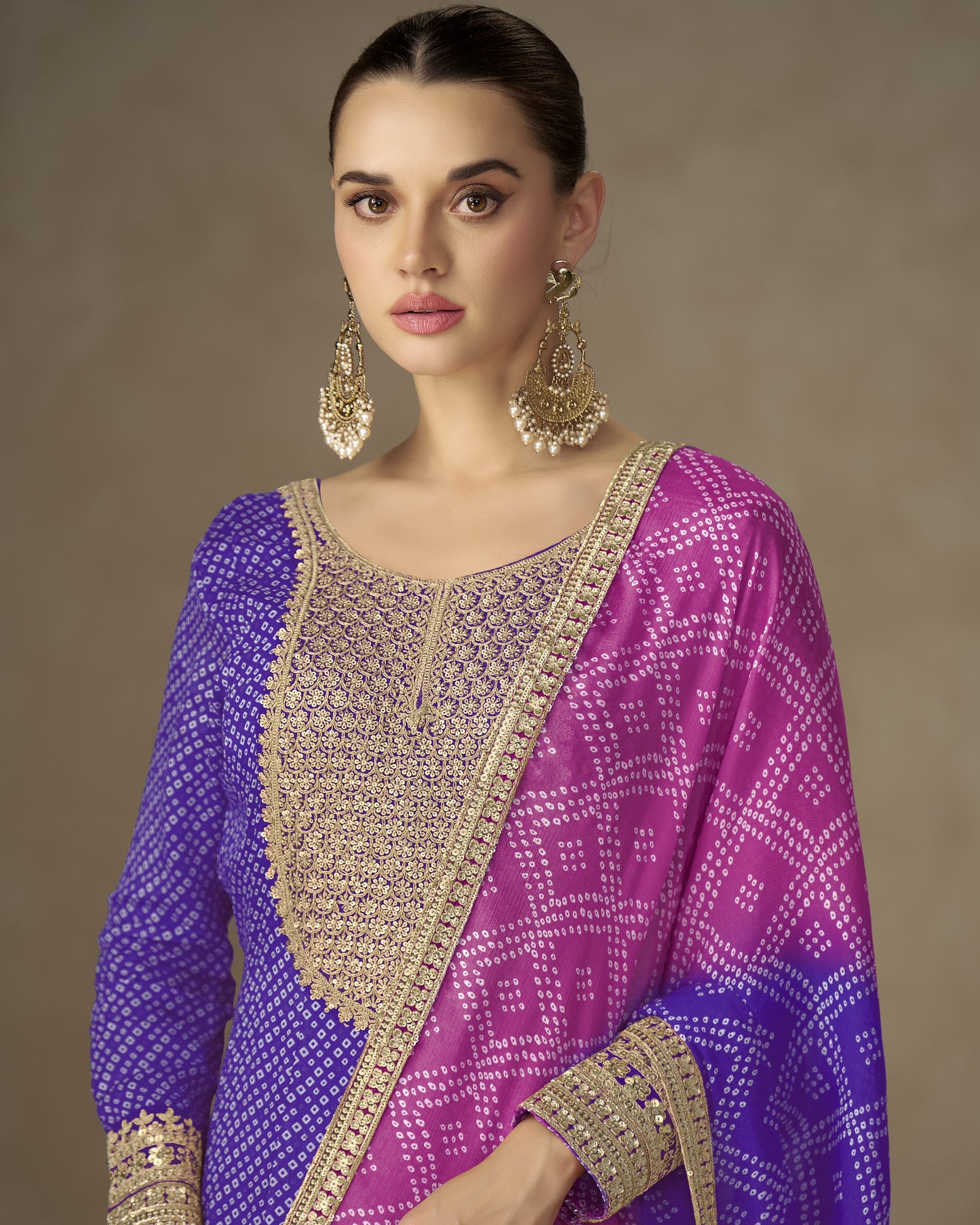 Woman wearing a purple and pink traditional outfit with gold embroidery against a brown background