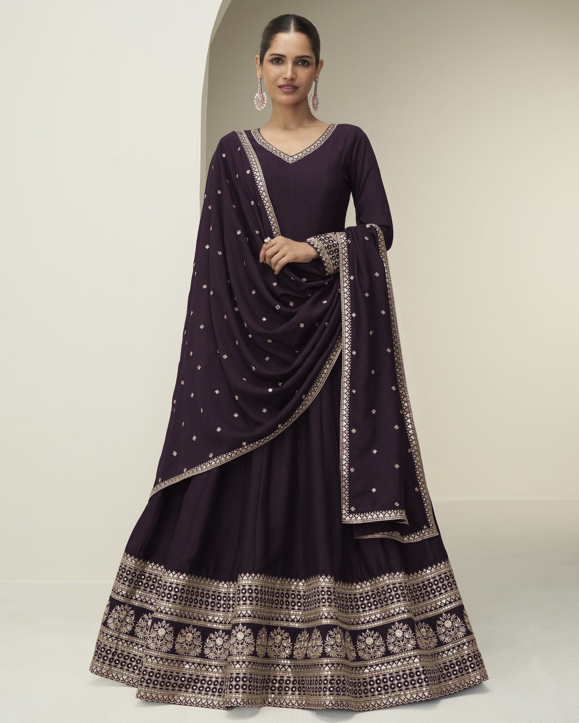 Woman wearing a dark purple traditional outfit with intricate patterns on a neutral background