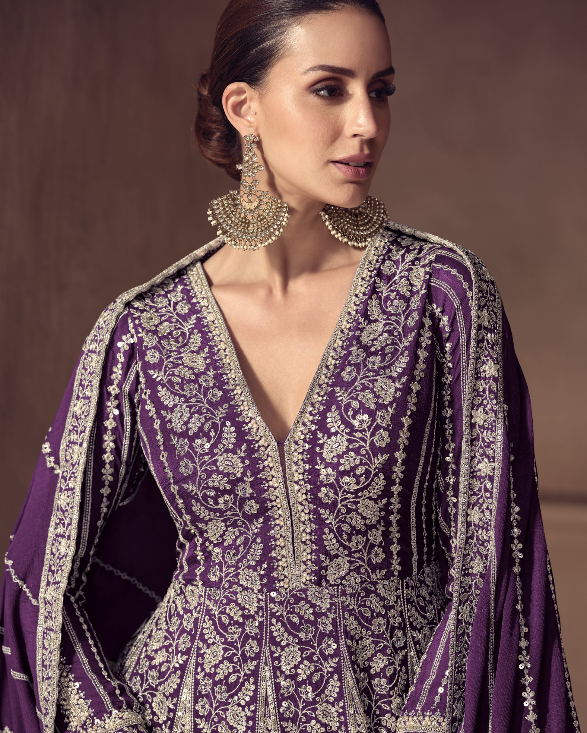 Woman wearing a purple embroidered dress with gold detailing against a brown background